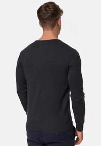 Pull gris foncé à manches longues et col rond. Poignets et ourlet côtelés, texture douce, design minimaliste sans logos ni embellissements.