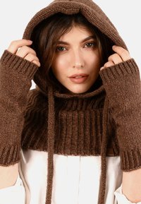 Tricou cu glugă tricotat de culoare maro, cu textură în dantelă, fără mâneci, și detalii cu șnur. Material moale cu un aspect cald.