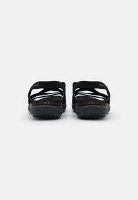 Musta pari Skechers-liukuvoimia, joissa on useita ristikkäisiä hihnoja, takahihna ja texturoitu pohja valkoista taustaa vasten.