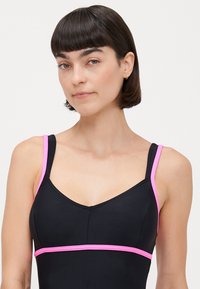 Maillot de bain noir avec des accents roses. Il présente des bretelles fines, un décolleté en V et une bande contrastante autour de la poitrine. Texture lisse, design ajusté.