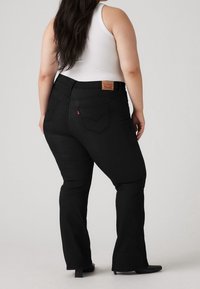 Jeans negros acampanados de tiro alto, hechos de mezclilla. Incluyen bolsillos traseros y una etiqueta de cuero con la marca en la parte trasera de la cintura.