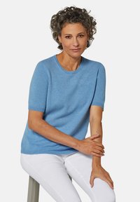 Helles blaues, kurzärmliges Sweatshirt aus einem weichen Stoff, mit Rundhalsausschnitt und gerippten Bündchen, kombiniert mit weißen Hosen.