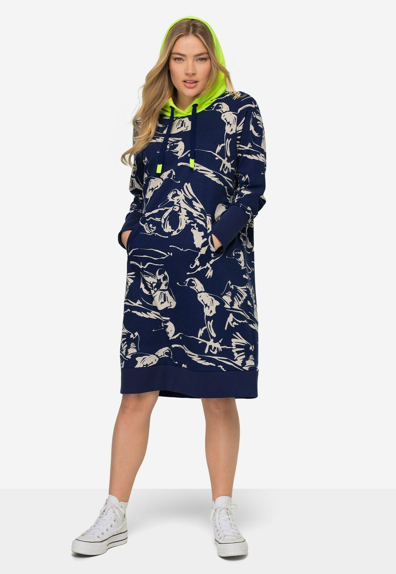 Robe à capuche navy avec des motifs abstraits blancs, poches avant et capuche vert fluo. Matière en mélange de coton, design mi-long et ourlet côtelé.