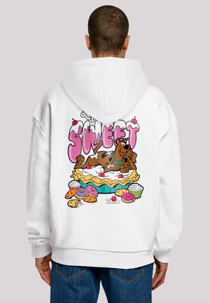 Hvit hettegenser med et fargerikt trykk på baksiden, som viser en tegneseriehund som slapper av på en pai omgitt av søtsaker, og teksten "SO SWEET."