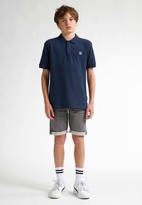 Tmavě modré polokošile s malým logem, doplněná o zrolované šedé šortky, bílé sportovní tenisky a pruhované ponožky.