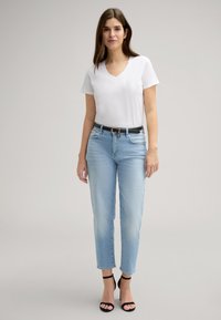 Witte V-hals t-shirt, lichtblauwe hoge taille jeans met rechte pijpen, zwarte riem met gouden hardware, en zwarte hoge hakken sandaaltjes.