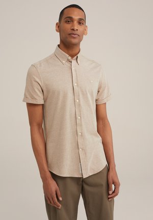 Beige Kurzarmhemd mit subtiler Textur, Knopfleiste und kleinem gesticktem Logo auf der Brust. Kombiniert mit olivgrünen Hosen.