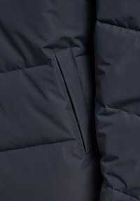 Marineblå dunjakke med quiltet design, der har en sidelomme og et glat, struktureret stof. Robuste syninger er synlige.