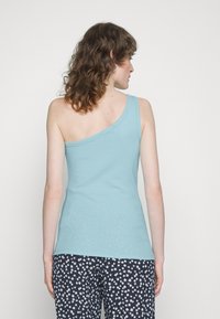 Top de alças azul claro, com um ombro só, com um design justo e tecido suave. Combinado com calças escuras estampadas com pequenas flores brancas.