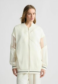 Weißer Bomberjacke mit transparenten Netzärmeln, goldenem Reißverschluss, Logo-Muster auf dem Netz und schwarzen gestreiften Bündchen. Glattes Material mit einem kastigen Schnitt.