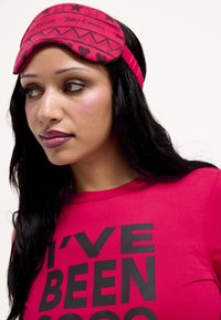 Piros alvómaszk csillag- és szívmintákkal, "Juicy Couture" márkajelzéssel, élénkpiros felsővel párosítva, amelyen vastag fekete felirat található.