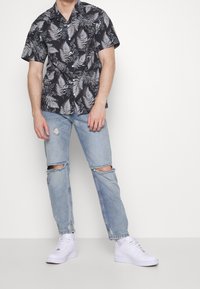Zwart shirt met korte mouwen en een wit varenspatroon, gecombineerd met lichtblauwe ripped jeans en witte sneakers, met een casual pasvorm.