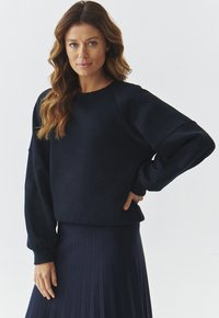 Sweat-shirt bleu marine avec un col rond, des manches raglan et un tissu texturé. Associé à une jupe plissée bleu marine.