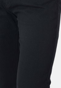 Pantaloni neri realizzati in tessuto testurizzato con un motivo sottile. Presentano un design slim fit e cuciture standard lungo i lati.