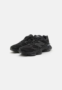 Black athletic shoes featuring mesh and suede materials, chunky design, textured surfaces, and reflective accents on the sides.