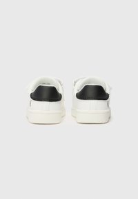 Baskets blanches avec une tige en toile lisse, un accent en cuir noir au niveau du talon, et une semelle en caoutchouc plate. Design minimaliste avec des coutures simples.