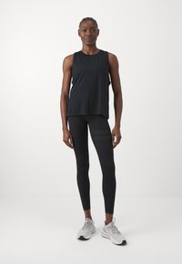 Haut de sport sans manches noir associé à des leggings noirs avec des accents texturés. Des chaussures de sport grises avec des semelles blanches complètent la tenue.