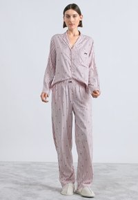 Conjunto de pijama rosa claro com riscas verticais, camisola de botões com mangas compridas e calças com cintura elástica. Apresenta um pequeno bolso e textura macia.