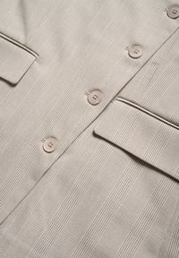 Blazer in tessuto beige con righe verticali, dotato di quattro bottoni, due tasche e una superficie in tessuto testurizzato.