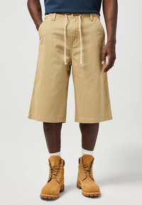 Pantalones cortos cargo caqui con un corte relajado, cinturilla con cordón, bolsillos laterales y dobladillo recto. Combinados con botas marrón claro y calcetines blancos de caña media.