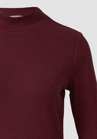 Geribbelde, langärmelige bordeaux trui met een hoge halslijn en subtiele textuur, getoond op het bovenste deel van de torso tegen een effen achtergrond.