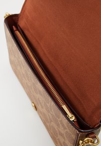 Braune Handtasche mit Muster, die einen goldenen Reißverschluss und ein weiches, hellbraunes Wildlederinterieur mit einer kleinen Reißverschlusstasche aufweist. Strukturierte Form und Lederakzente.