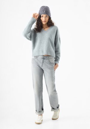 Light blue, cropped, v-neck sweater in soft fabric; paired with light gray, rolled-cuff jeans and off-white sneakers. Gray knit beanie worn.