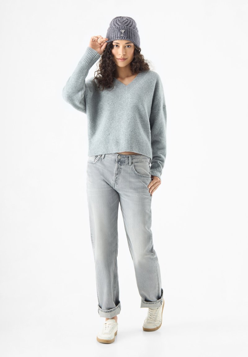 Lichtblauwe, cropped, v-hals trui van zachte stof; gecombineerd met lichtgrijze jeans met opgerolde manchetten en off-white sneakers. Grijze gebreide beanie gedragen.
