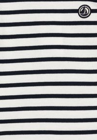 Svart og hvit horisontalstripet stoff med en teksturert strikk. Har en liten, sirkelformet brodert logo i øverste høyre hjørne.