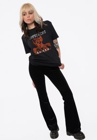 Black graphic t-shirt with "Offspring" and "SMASH" printed in orange and white; paired with flared black velvet pants and black ankle boots.