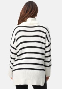 Pull rayé noir et blanc avec col montant, coupe ample et ourlet côtelé. Le tissu semble tricoté, avec une finition texturée.