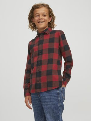 Camicia di flanella a quadri rossi e neri con maniche lunghe e chiusura a bottoni, abbinata a jeans in denim blu. Tessuto morbido, colletto standard.