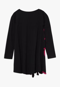 Czarna sukienka z długim rękawem, z okrągłym dekoltem, asymetrycznym dołem i różowymi dekoracyjnymi frędzlami po bokach. Miękka tekstura materiału.