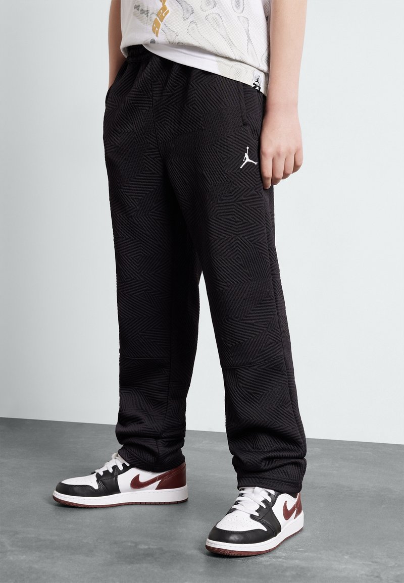 Pantaloni jogger neri con un motivo geometrico testurizzato, dotati di una cintura elastica e un piccolo logo Jordan bianco. Abbinati a sneaker nere e bianche.