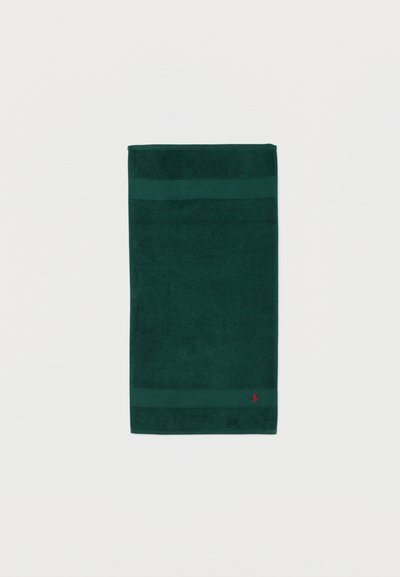 Σκούρα πράσινη διπλωμένη πετσέτα με δύο οριζόντιες ρίγες κοντά στις άκρες και μικρό κόκκινο κεντημένο λογότυπο στο κάτω δεξί μέρος.