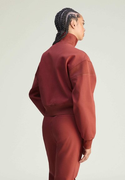 Bordowa krótka bluza z wysokim kołnierzem, długimi rękawami i poziomym przeszyciem. W parze z dopasowanymi bordowymi spodniami. Gładka tekstura.