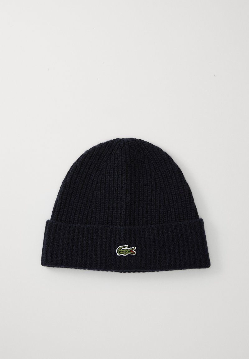 Sötétkék kötött sapka bordázott textúrával és hajtott mandzsettával, az elején egy kis hímzett krokodil logóval.
