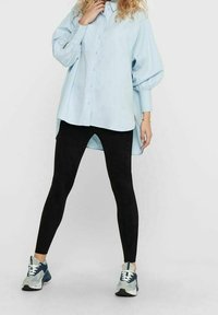 Camicia oversized azzurro chiaro con maniche a palloncino, abbinata a leggings neri. Modella che indossa scarpe da ginnastica blu e grigie.