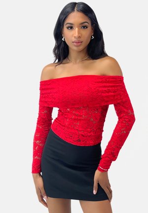 Top rosso in pizzo, scollato sulle spalle e con maniche lunghe, caratterizzato da motivi floreali. Abbinato a una mini gonna nera aderente. Texture liscia.