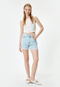 Pantalones cortos de mezclilla azul claro con dobladillo deshilachado, que presentan patrones de costura en diagonal. Combinados con una camiseta corta blanca de canalé y zapatillas blancas sin cordones.