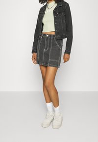 Sort denimjakke, lysegrøn cropped top, sort denimnederdel med hvid syning, hvide sokker og kraftige hvide sneakers.