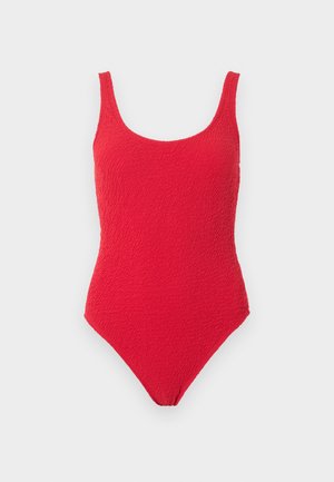 Maillot de bain une-pièce rouge texturé avec larges bretelles et encolure arrondie sur un fond uni.