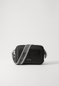 Musta olkalaukku, jossa on teksturoidusta kankaasta valmistettu runko, sileä nahkainen etuosa ja kontrastivärinen hihna, jossa on "MICHAEL KORS" -brändäys.
