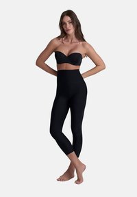 Collant neri senza cuciture con vita alta, realizzati in un materiale morbido ed elasticizzato, abbinati a un reggiseno nero senza spalline.