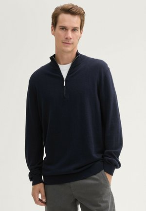 Granatowy sweter z zamkiem przy kołnierzu, wykonany z miękkiego materiału. Długie rękawy z ribbingu przy mankietach i u dołu, co doskonale uzupełnia casualowy wygląd.