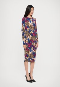 Getailleerde jurk met lange mouwen in een bloemen- en luipaardprint, met levendige tinten van roze, blauw en beige, aangevuld met hoge zwarte hakken.