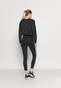 Felpa nera con motivo a righe e polsini a coste, abbinata a leggins neri con strisce bianche sui lati. Il modello indossa scarpe da ginnastica nere.