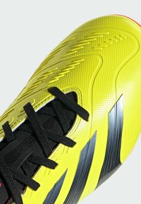 Scarpe da calcio gialle con tomaia texturizzata, lacci neri e accenti a striscia argentata. Forma curvilinea con finitura lucida.