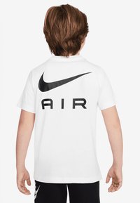 T-shirt bianco in cotone con un grande logo Nike swoosh nero e la parola "AIR" stampata sul retro in lettere maiuscole.