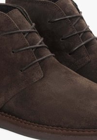 Brązowe zamszowe buty chukka z okrągłym noskiem, detalami wiązania i szytą podeszwą. Gładka faktura i klasyczny design.